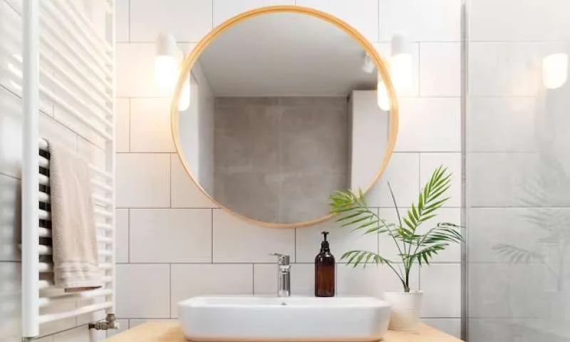 Round wood-framed mirror above a white basin in a tiled bathroom.