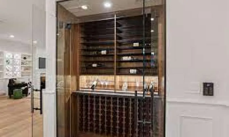 Glass-enclosed wine cellar with timber racking, seen through its framed glass door.