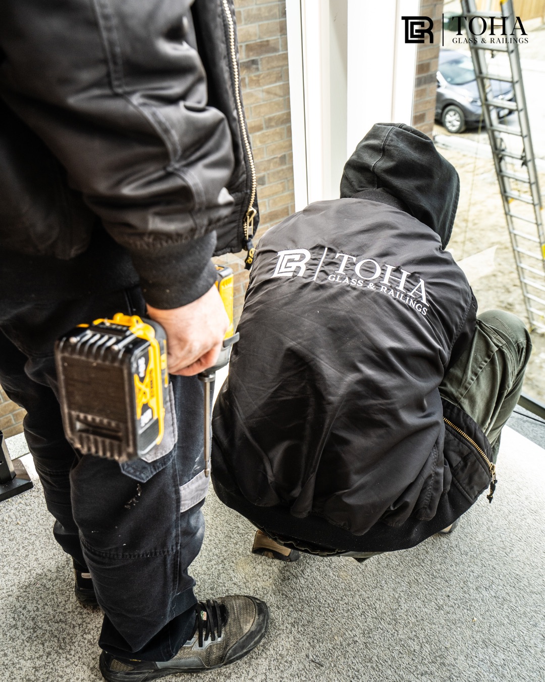 Two Toha Glass installers in branded workwear fitting a glass panel on site.