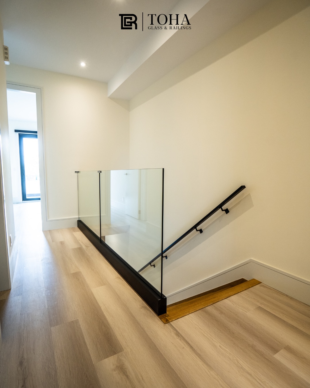 Base shoe glass railing with a slim black handrail at an upstairs landing.