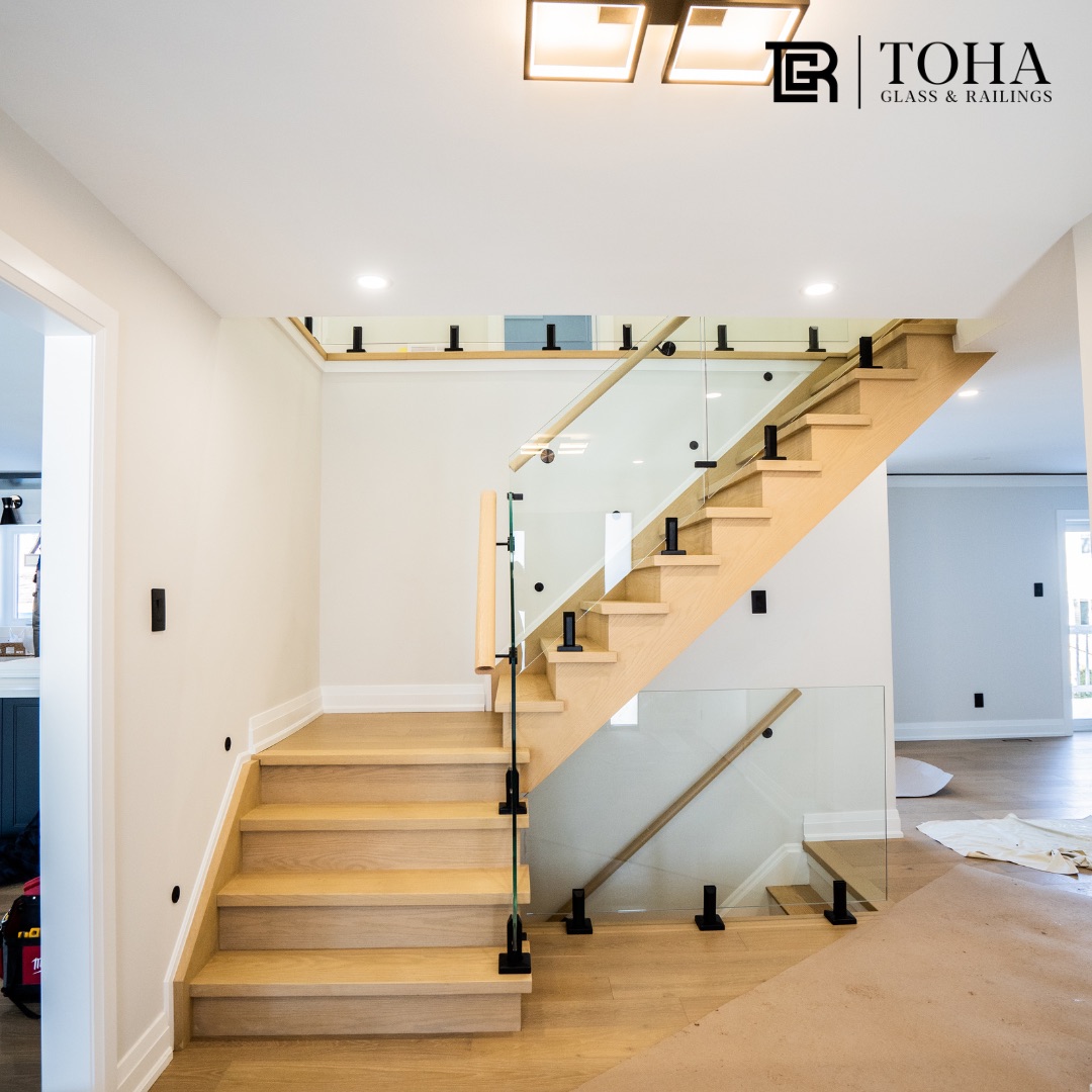 Glass staircase railing with black fixings beside a pale oak stair in a new build.